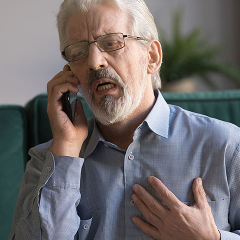 Elderly man talking on phone while holding his chest